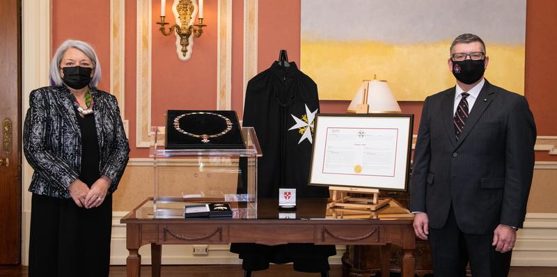 The Governor General and a man stand on either side of a table that features medals, decorations and a certificate.