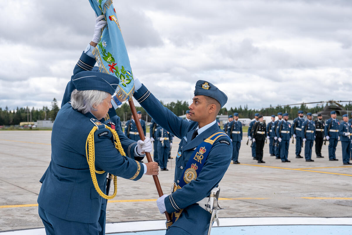 La gouverneure générale Mary Simon tient l’étendard et le remet à un membre des Forces armées canadiennes