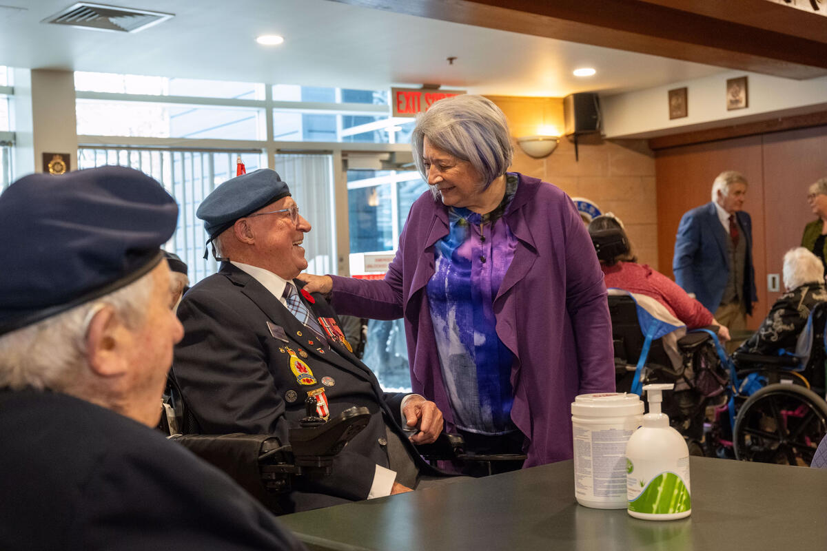 La gouverneure générale Mary Simon s'entretient avec un vétéran de l'Aviation royale canadienne assis dans un fauteuil roulant