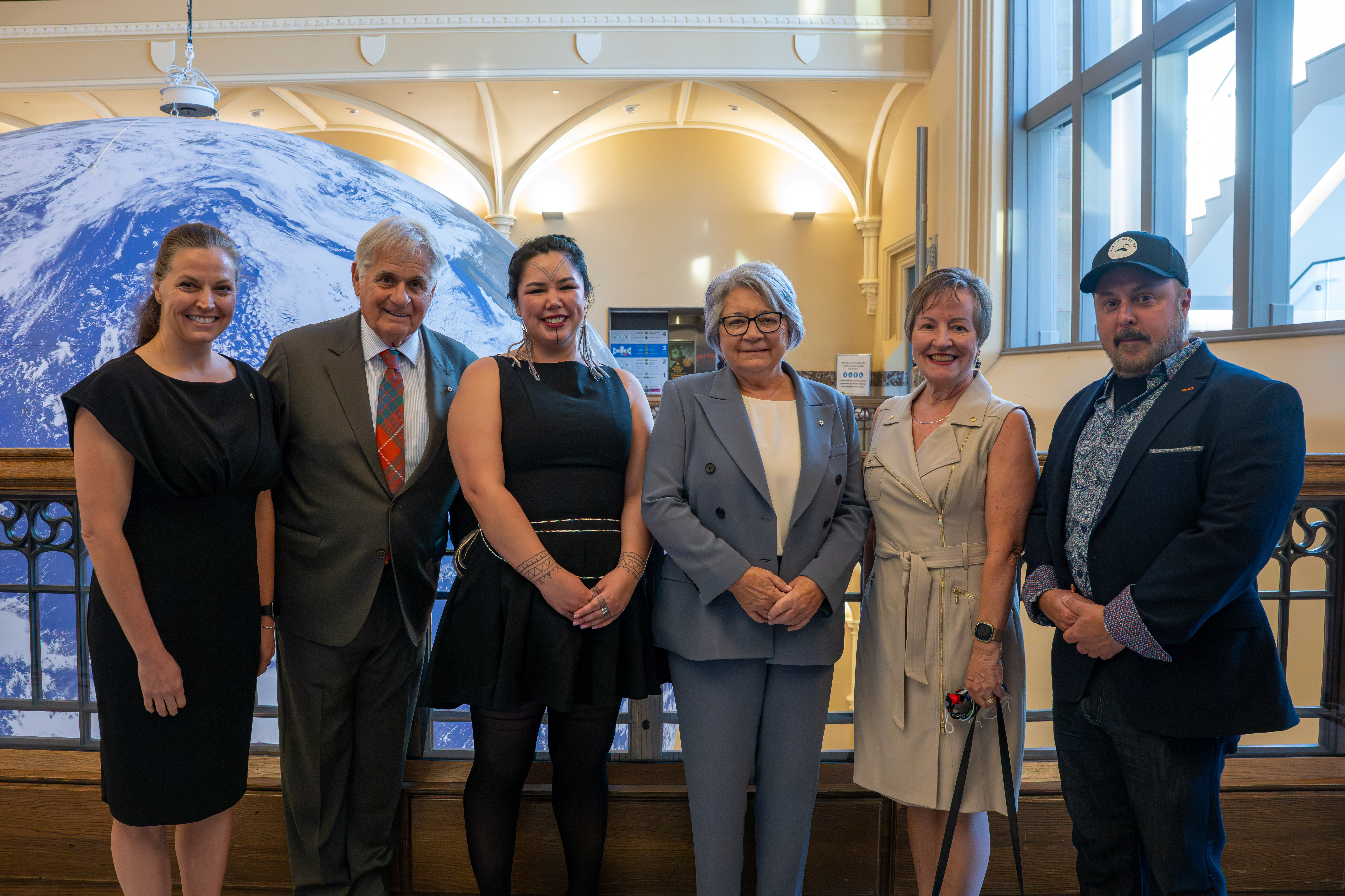 Governor General Mary Simon and Mr. Whit Fraser posing for a picture with four other people inside the Nature Museum.