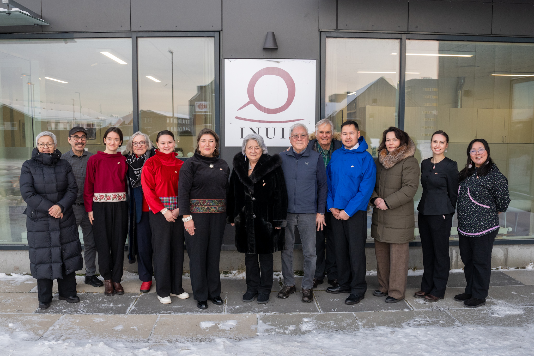 La gouverneure générale Mary Simon et M. Whit Fraser debout à l'extérieur avec un groupe de personnes. Derrière eux, un panneau porte l'inscription « Inuit ».