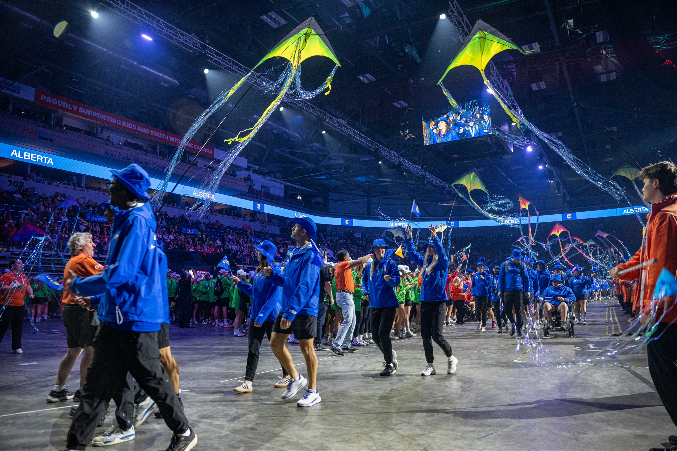 Des athlètes marchent dans un grand stade. De grands cerfs-volants volent au-dessus d'eux.