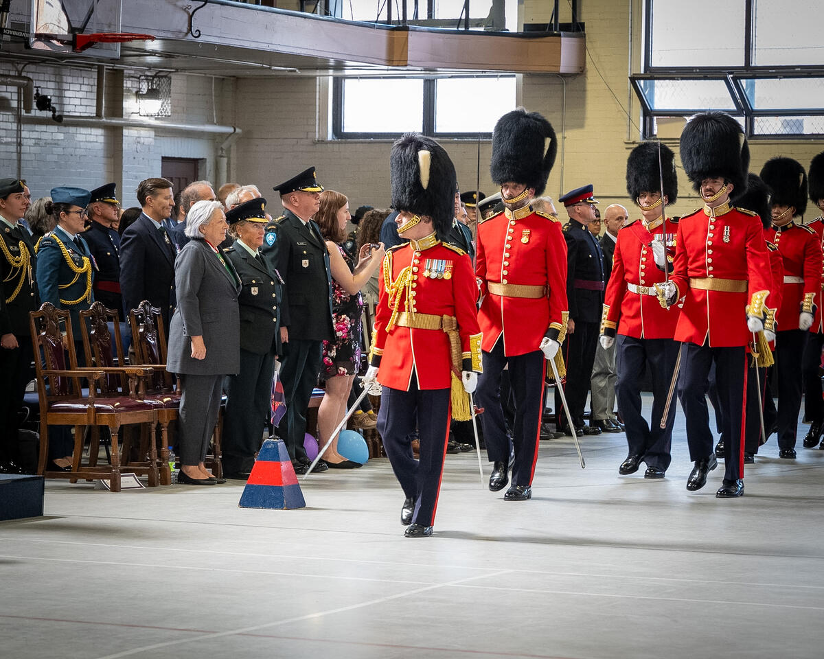 Governor General Mary Simon standing with a group of people as the Canadian Grenadier Guards pass. They are in a large gymnasium.