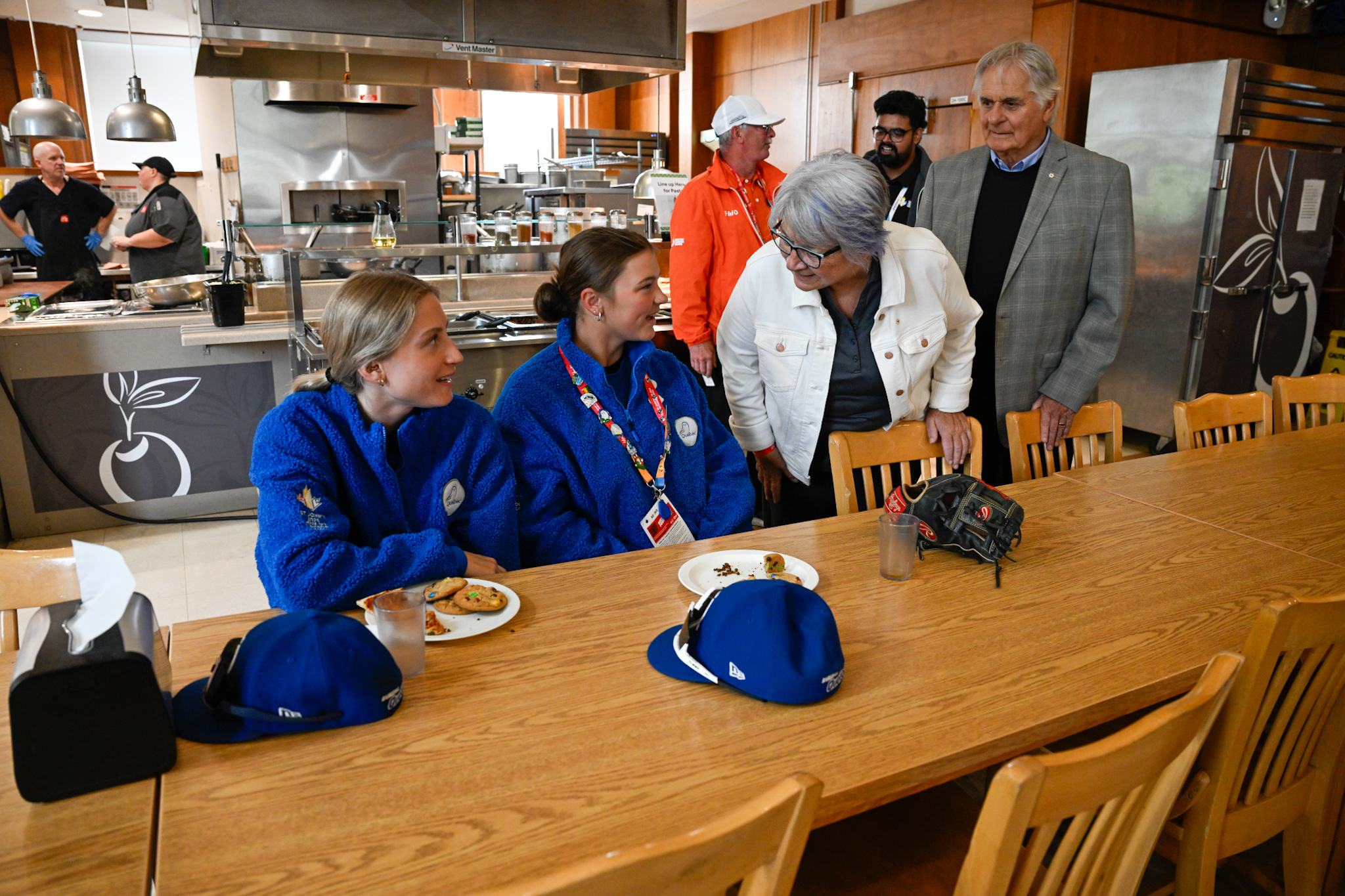 La gouverneure générale Mary Simon et M. Whit Fraser s'adressent à deux jeunes gens vêtus de polaires bleues à fermeture éclair, assis à une longue table devant laquelle se trouvent des assiettes.