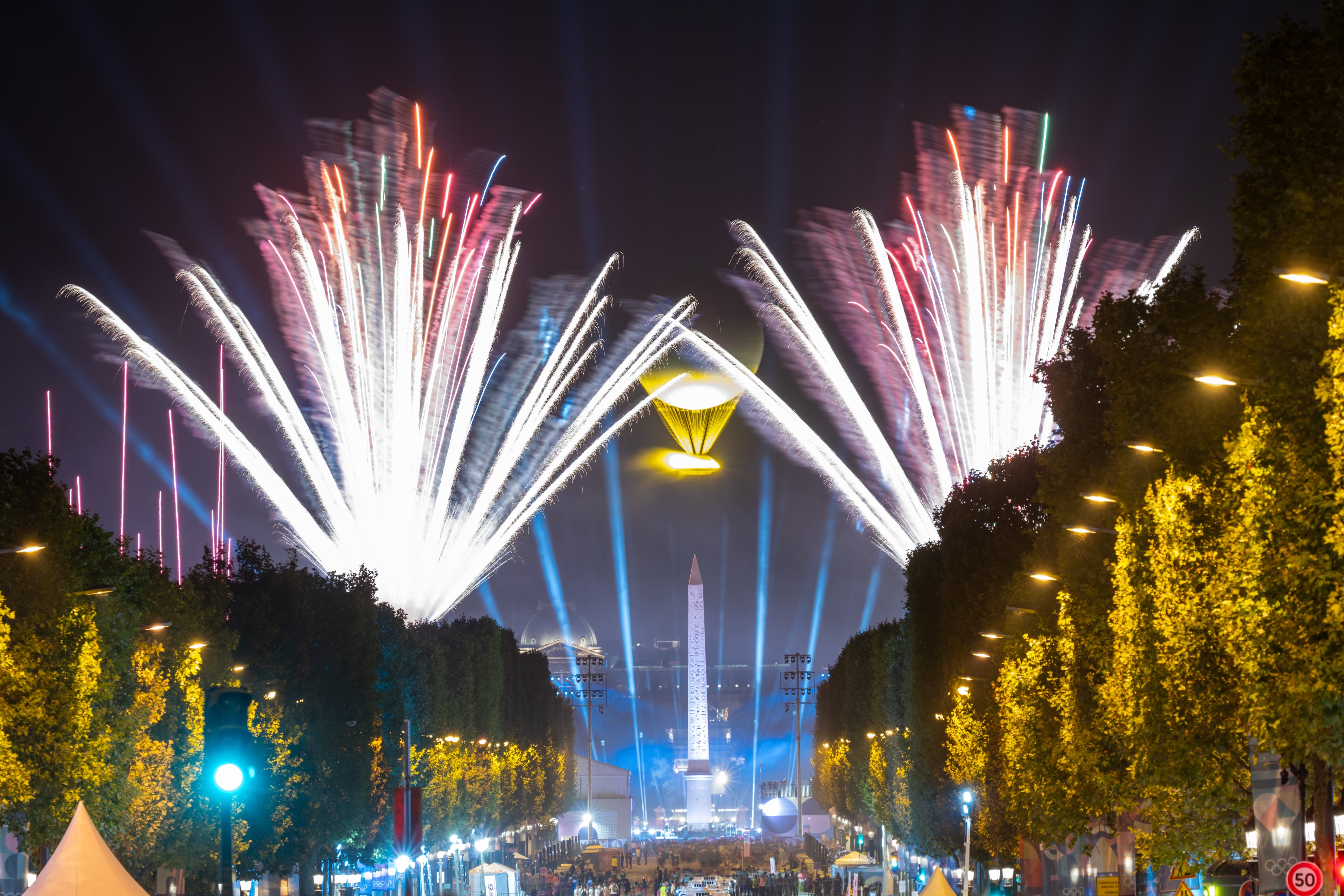 Vue des Champs-Élysées la nuit. Le ciel est illuminé par des feux d'artifice.