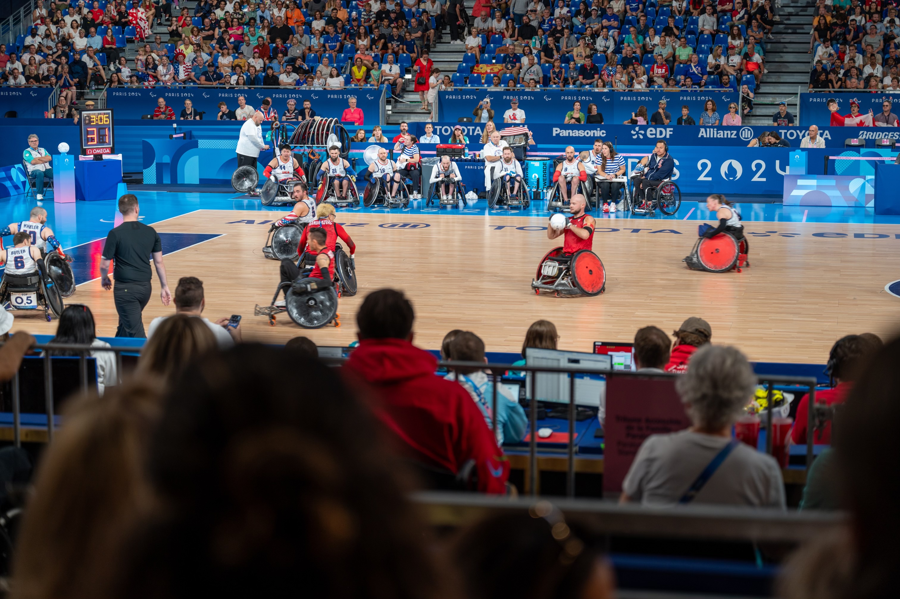 Un match de rugby en fauteuil roulant dans une grande arène intérieure remplie de spectateurs.