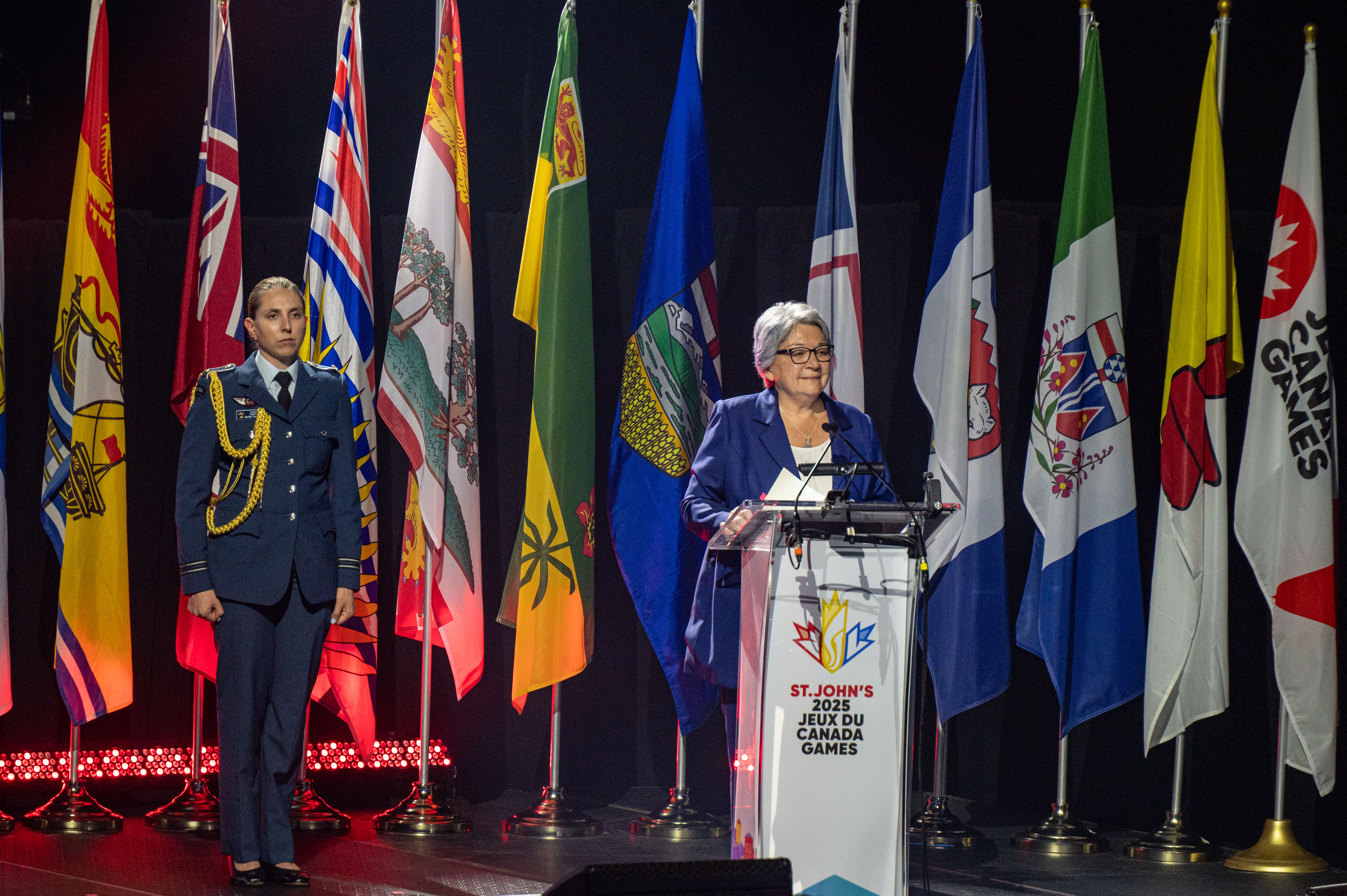 La gouverneure générale Mary Simon debout à un pupitre. Derrière elle, des drapeaux provinciaux. À sa droite, une femme en uniforme militaire.