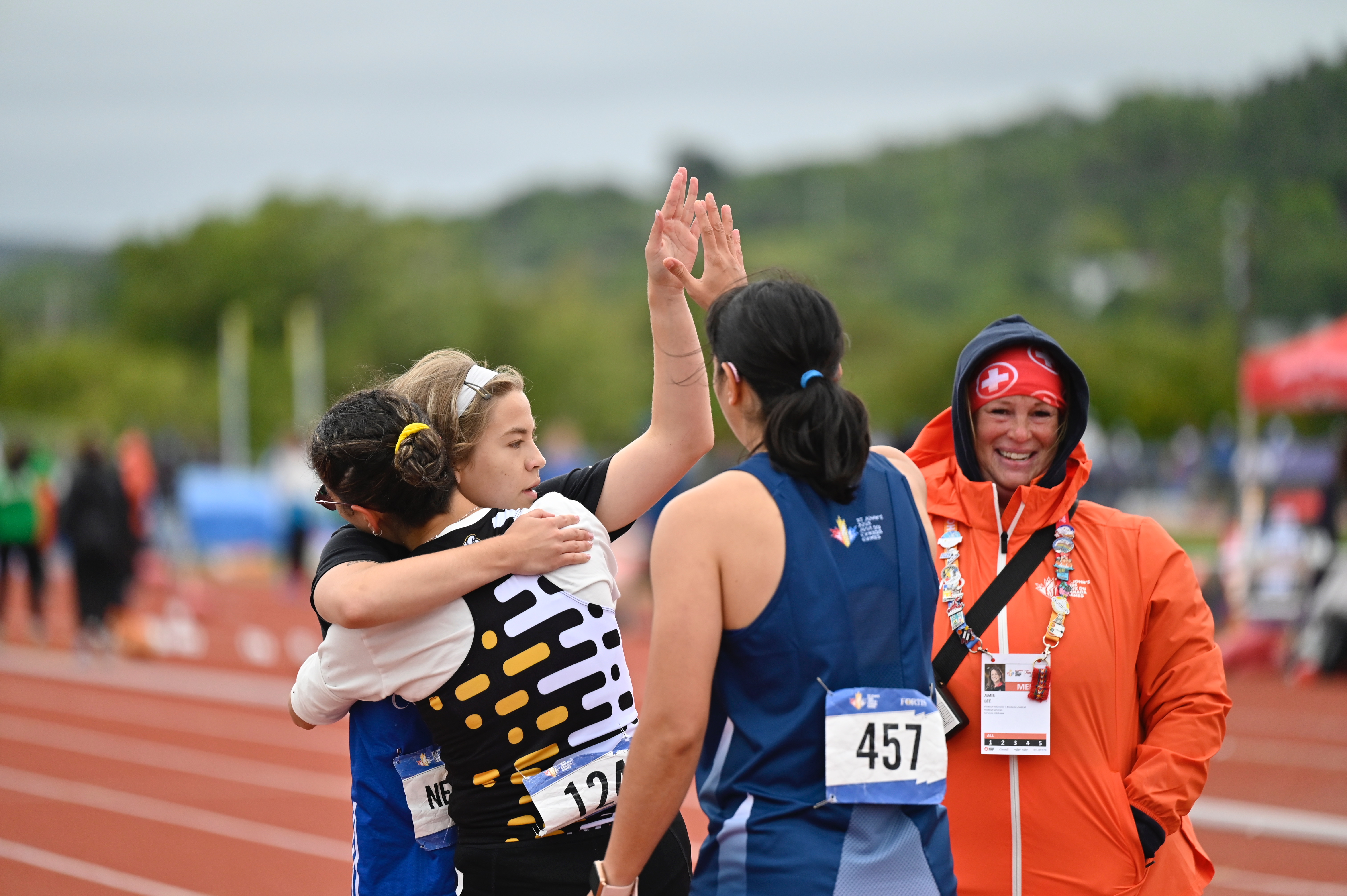Des athlètes s'étreignent et se tapent dans la main sur la piste d'athlétisme. Un secouriste vêtu d'une veste orange se tient près d'eux.