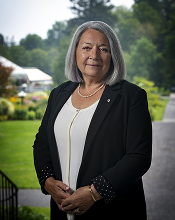 Official photo of Governor General Mary Simon. She is outdoors. The Rideau Hall gardens are visible in the background.