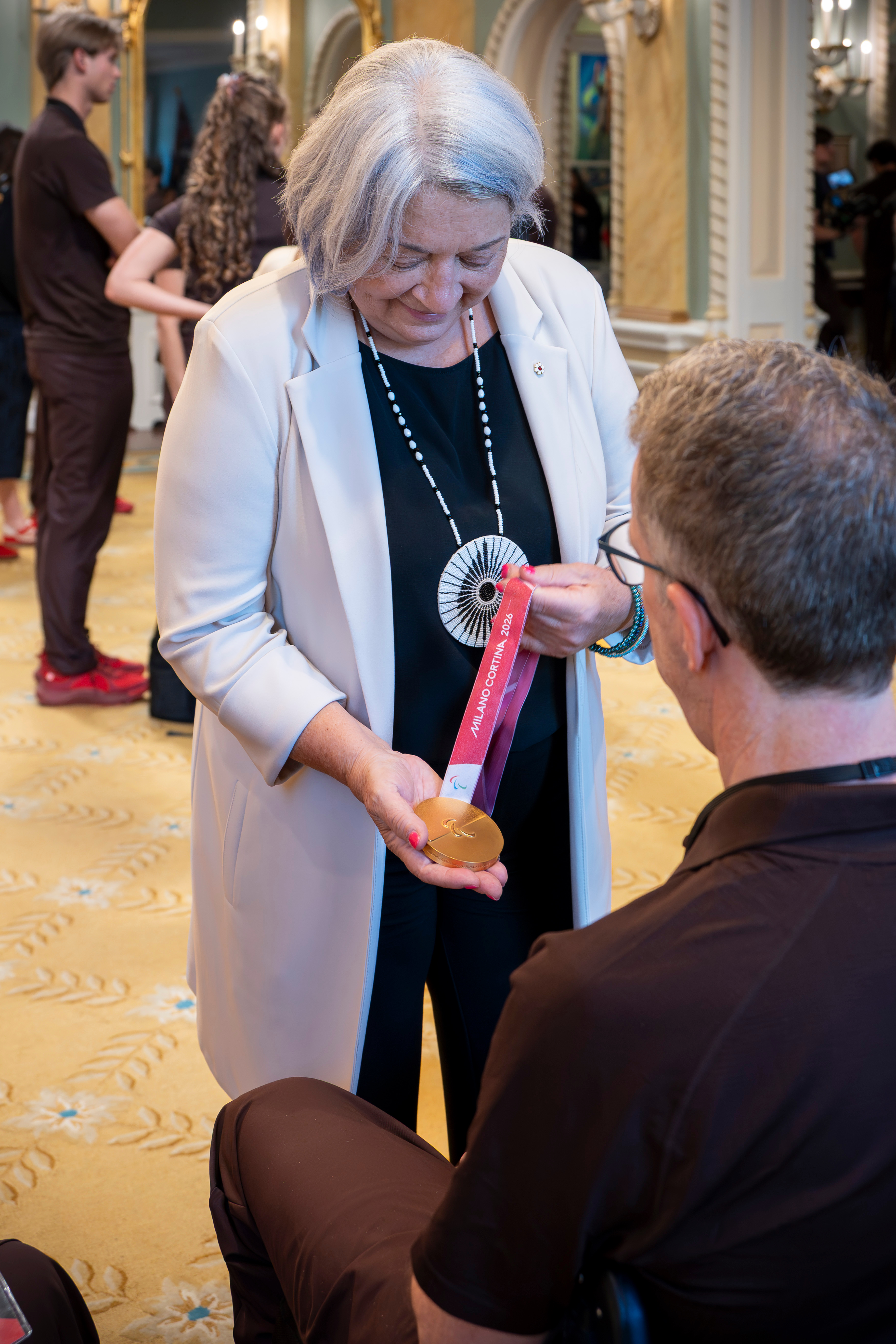 Governor General Mary Simon holding an Olympic medal. A person is seated in front of her.