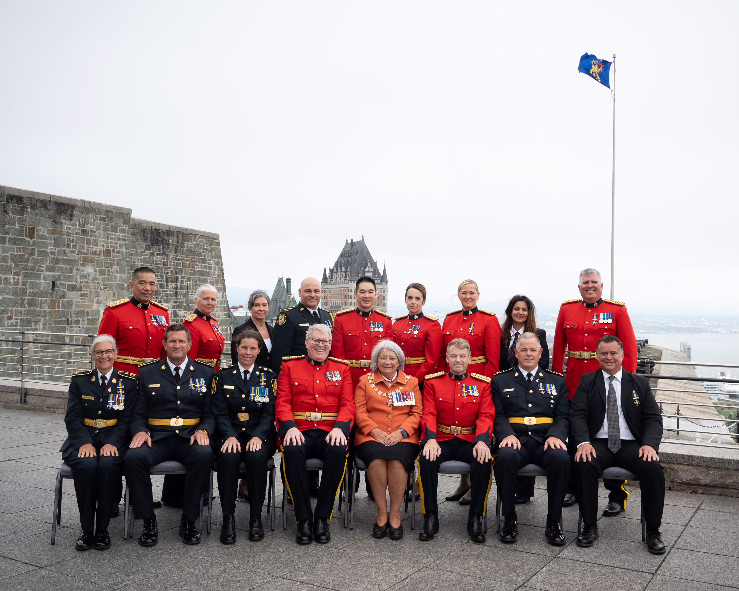 A group of police officers in ceremonial uniforms sitting on chairs outside with the Governor General.