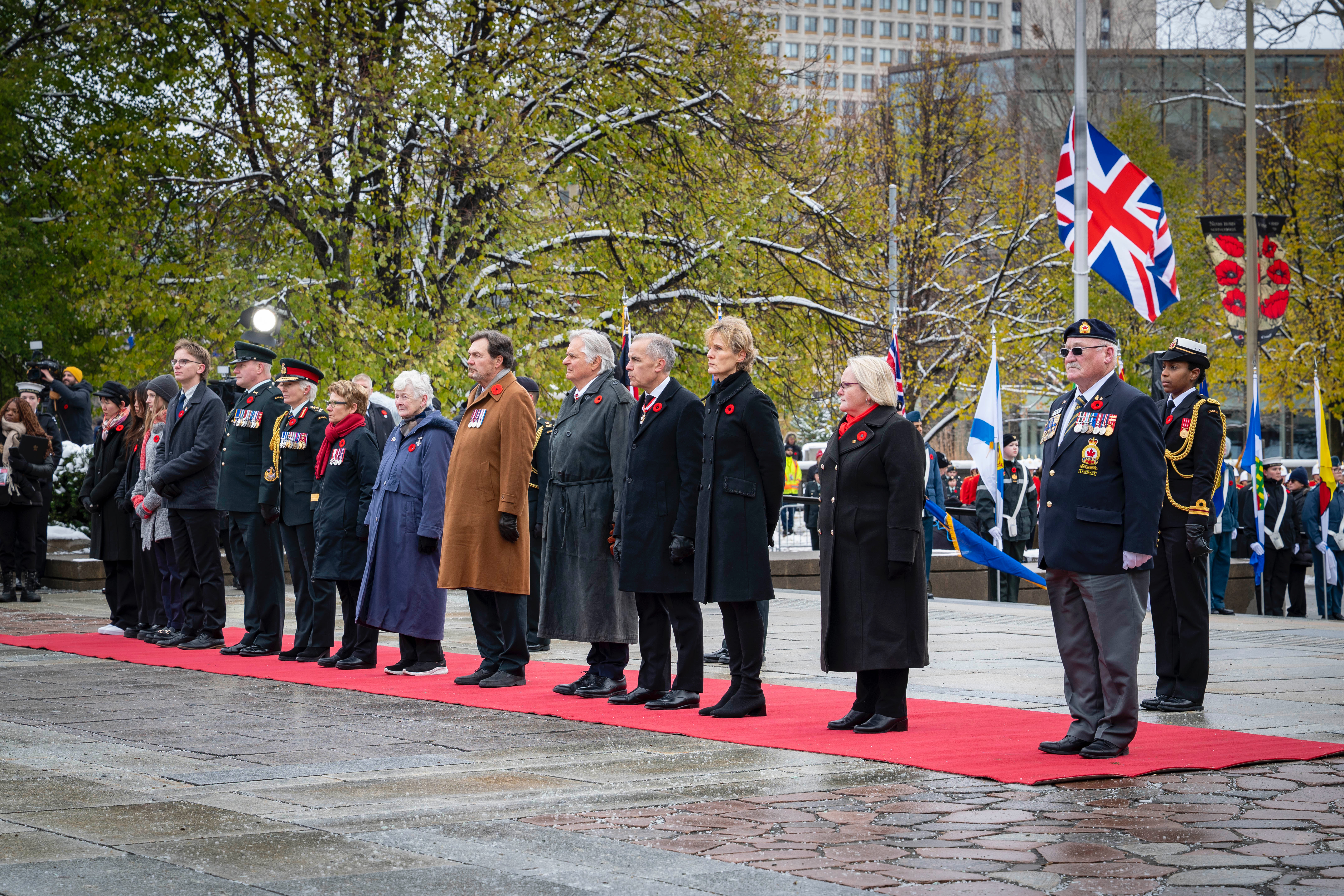 A row of people standing on a red carpet during a Remembrance Day ceremony.