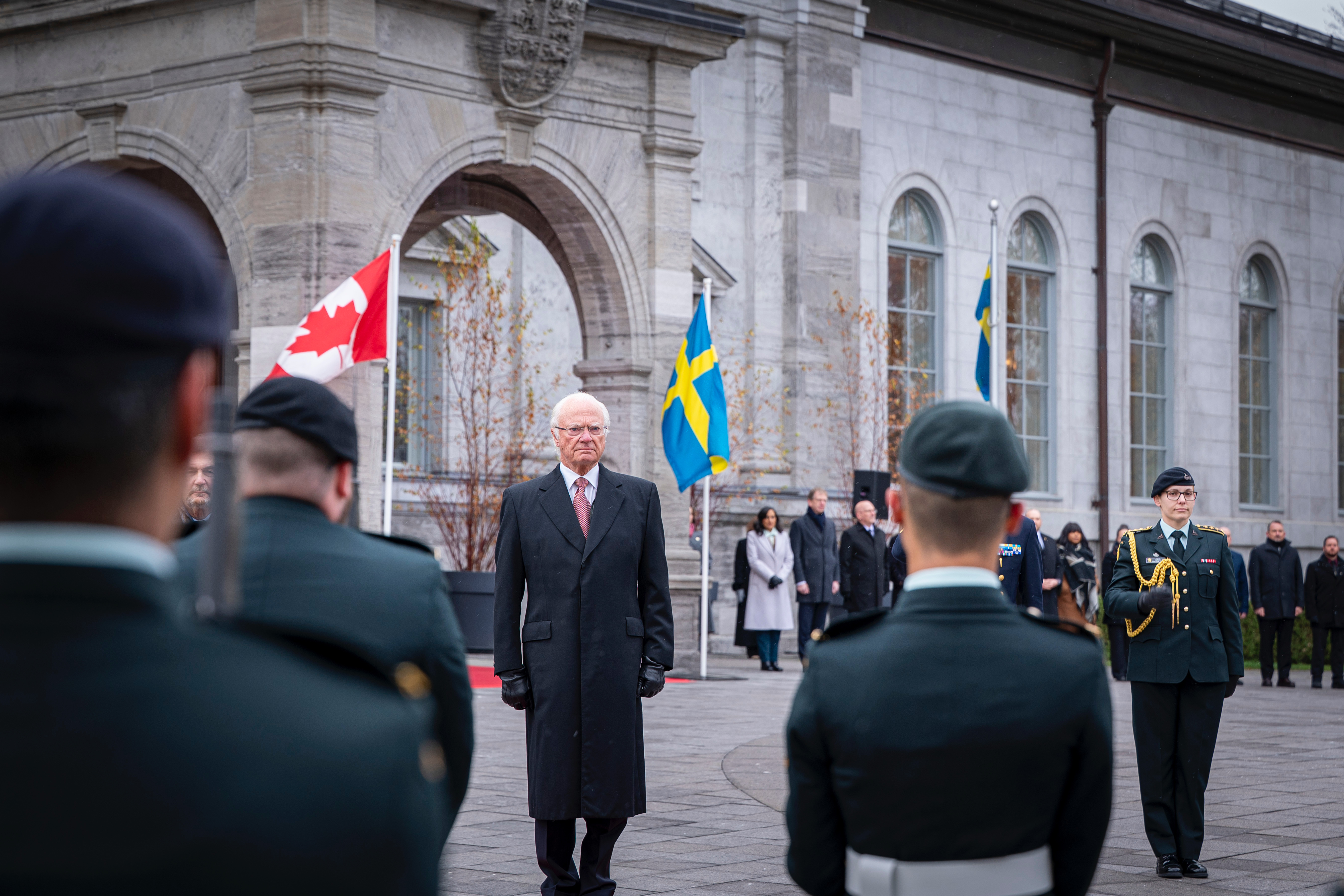 Sa Majesté le roi Carl XVI Gustaf debout sur une estrade devant une garde d'honneur.