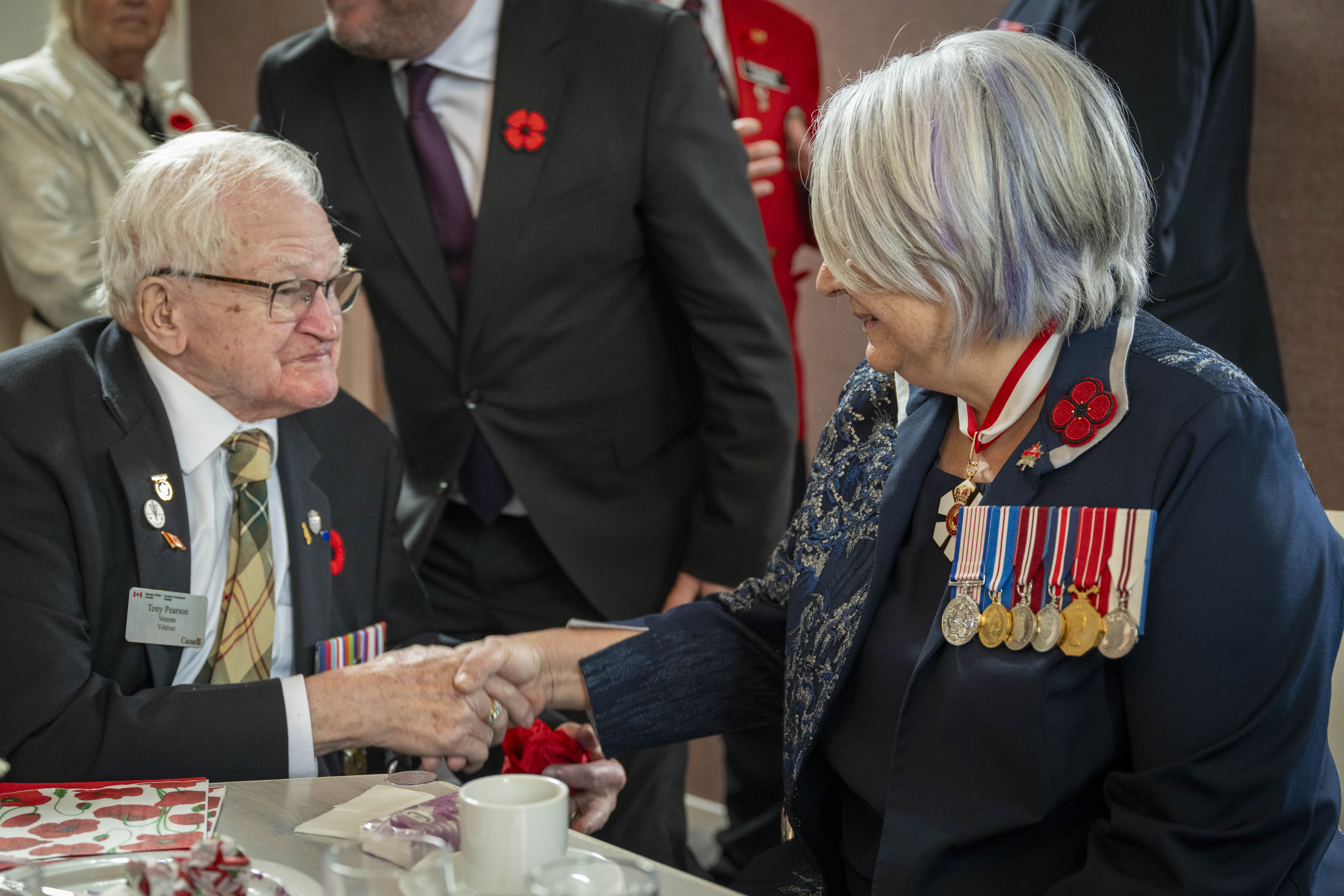 La gouverneure générale Mary Simon, assise à une table, serrant la main avec un ancien combattant canadien.
