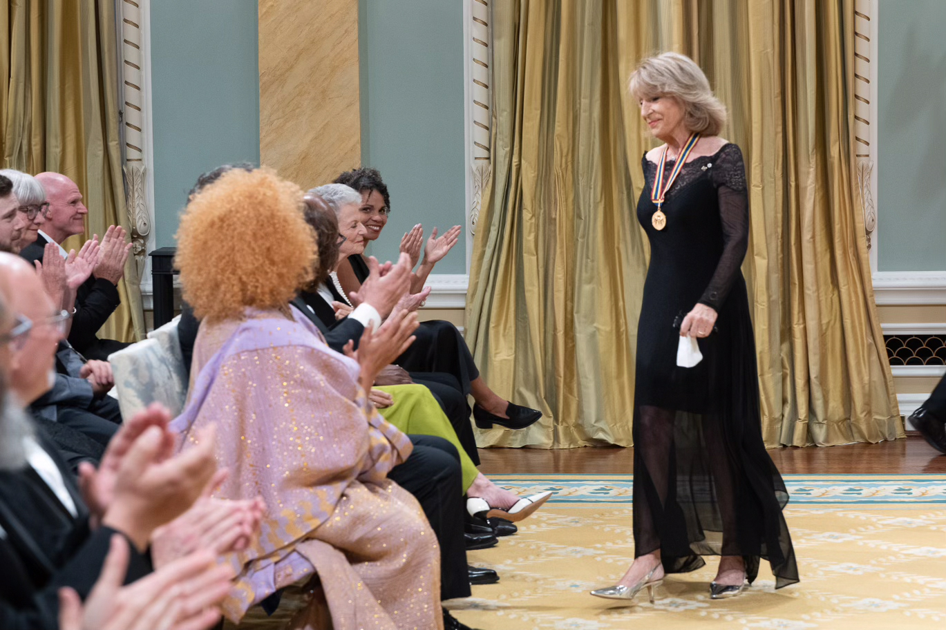 Diane Juster return to her seat while the audience applauds in the Ballroom at Rideau Hall