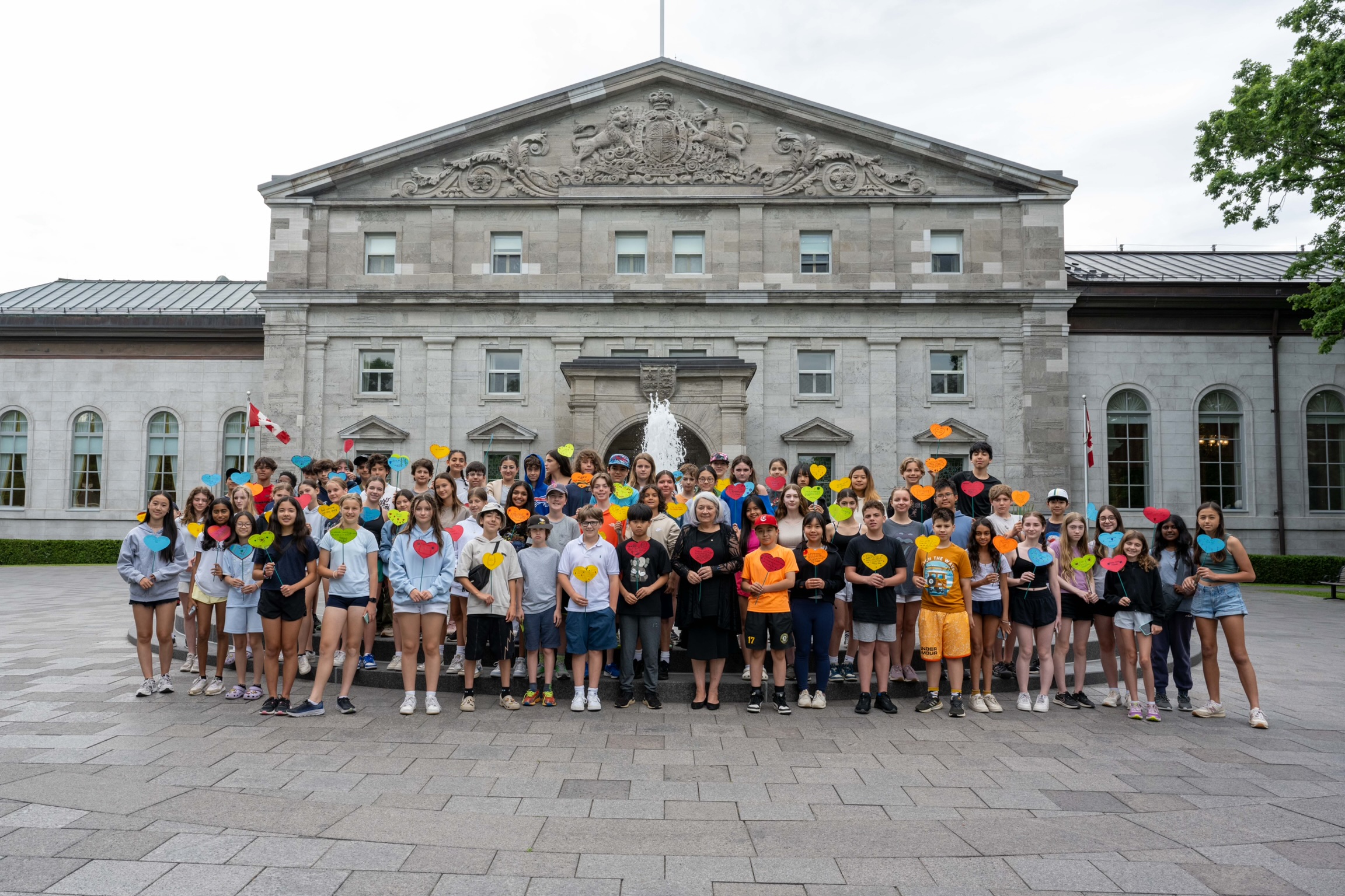 Governor General Mary Simon stands with a large group of students in front of the Rideau Hall fountain.