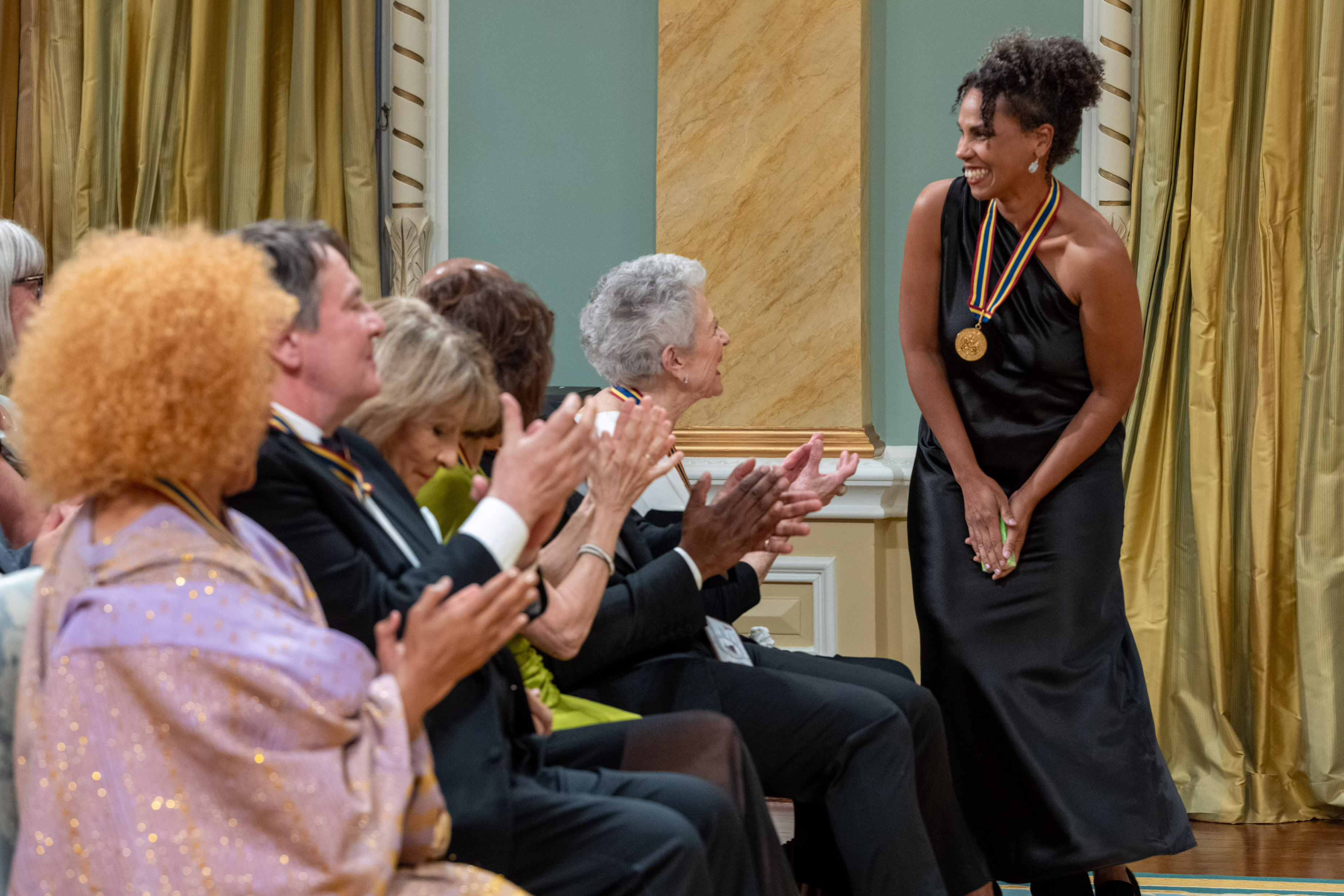 Mélanie Demers stands and smiles while the audience applauds her in the Ballroom at Rideau Hall