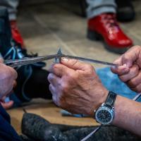 A close up of a man’s hands with a knife and a rope.