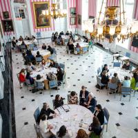 A view from the top of the Tent Room at Rideau Hall shows groups of women sitting at round tables. They are all engaged in discussion.
