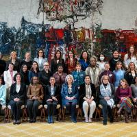A group of approximately 40 women pose with Governor General Simon for a photo in the Ballroom at Rideau Hall. They are gathered in front of a large painting.