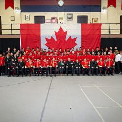 La gouverneure générale Mary Simon et un grand groupe de militaires et de civils posent pour une photo de groupe devant un drapeau canadien. Le groupe comprend des soldats assis et debout, alignés en rangées, dans un grand gymnase.