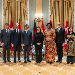 Photo de groupe avec l'honorable Suzanne Côté et six nouveaux chefs de mission, avec les drapeaux de chaque pays derrière eux. Deux gardes d'honneur se trouvent à l'arrière.