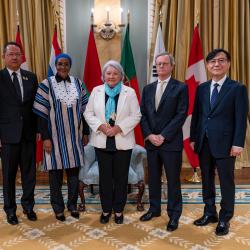 La gouverneure générale Simon aux côtés de quatre nouveaux chefs de mission, avec les drapeaux de chaque pays derrière eux et les drapeaux du Canada à chaque extrémité.