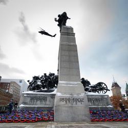 Le Monument commémoratif de guerre à Ottawa. Plusieurs couronnes sont déposées au pied du monument. Un hélicoptère est visible dans le ciel.