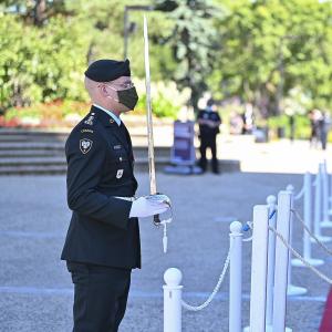 A military member in service dress holds a sword in front of him. A woman dressed in white is standing in front of him.