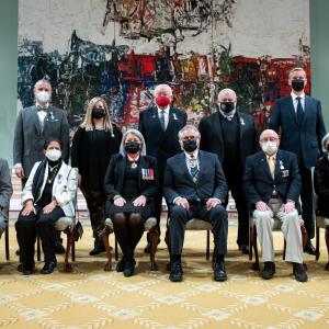 A group of eleven people, six sitting at the front and five standing behind, are posing for a photo in front of a large painting.