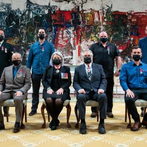 A group of eight people, four sitting at the front and four standing behind, are posing for a photo in front of a large painting.