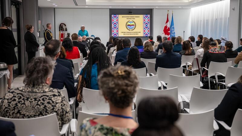 Governor General Mary Simon speaking to members of the Canadian delegation. People are seated in white chairs. A projector at the front of the room has the words "United Nations Permanent Forum on Indigenous Issues" on the screen.