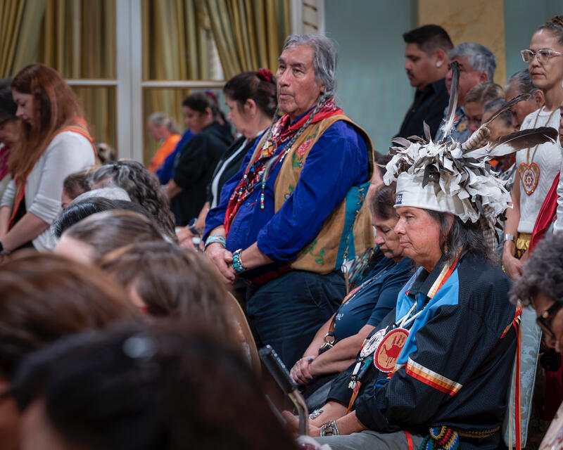 People in regalia stand and sit in a room