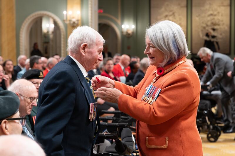 Governor General Mary Simon pinning a poppy to a veteran’s suit jacket.