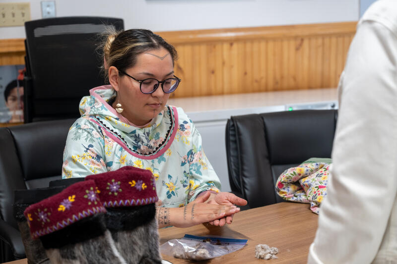 Une femme assise à une table. Elle tient quelque chose entre ses mains.