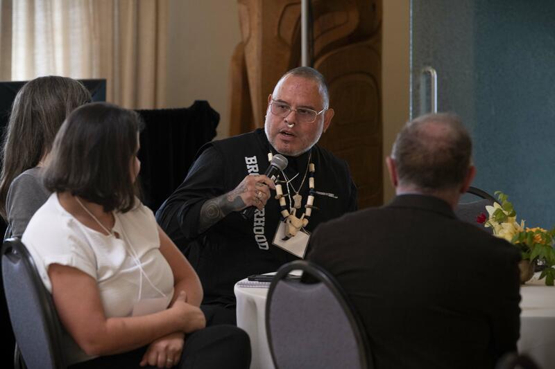 People sitting at a table. One person is holding a microphone.