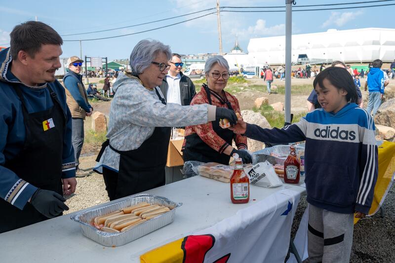 Governor General Mary Simon serves a hotdog to a young visitor at Nunavut Day celebrations