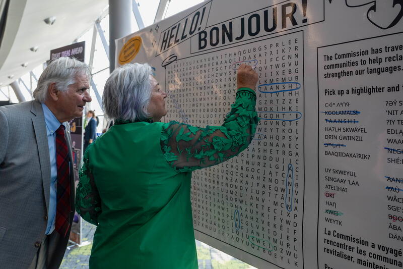Two people standing in front of a large crossword puzzle on a wall.