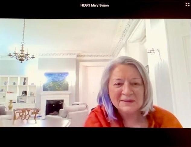 Screenshot of Governor general Mary Simon participating in a virtual event. She is smiling and wearing an orange shirt. A chandelier and fireplace are visible in the background.