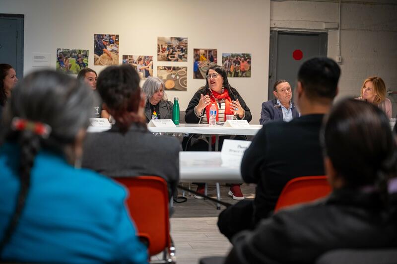 A diverse group of people engaged in a discussion around a table. The walls feature colourful photos.