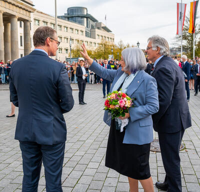 Her Excellency with a bouquet of flowers waving to a crowd.