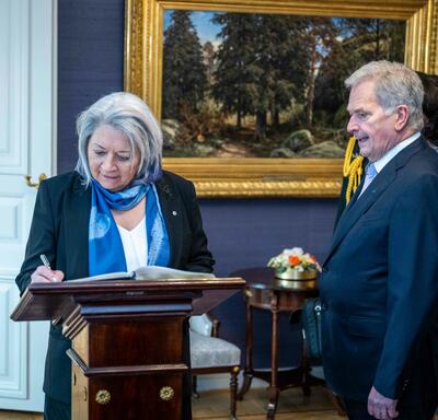Governor General Simon signing a guest book. President Sauli Niinistö is standing to her right.