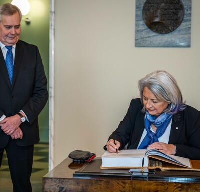 Governor General Simon signing a guest book. First Deputy Speaker Antti Rinne is standing to her right.