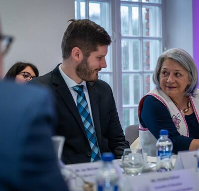 Governor General Simon sitting at a large table, smiling to a man on her right.