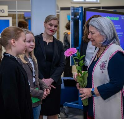 Governor General Simon holding a pink flower and speaking to two school children. Two women are standing behind them.