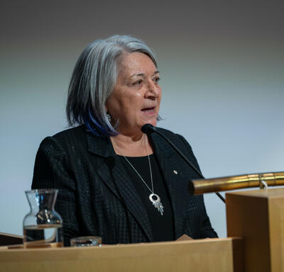 Governor General Simon standing at a podium and addressing a crowd.  
