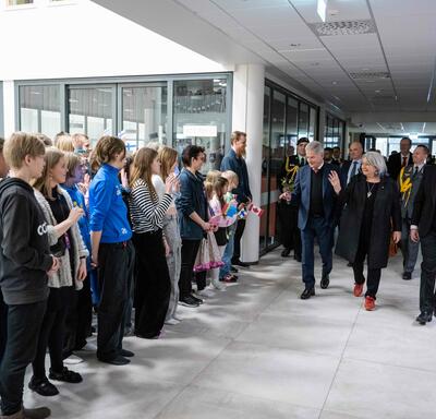 Governor General Simon walking inside a building and smiling at students. There are people standing behind her. The students are holding flags of Finland and Canada. 