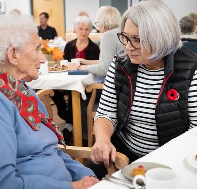 The Governor General chats with a woman. They are seated at a dining table.