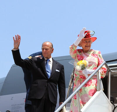 La reine et le duc d’Édimbourg saluent le public du haut d’un escalier blanc. Ils se tiennent devant la porte ouverte d’un avion.
