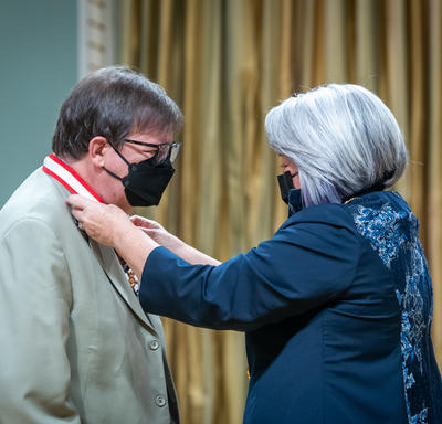 The Governor General is placing a medal around Rémy Girard’s neck.